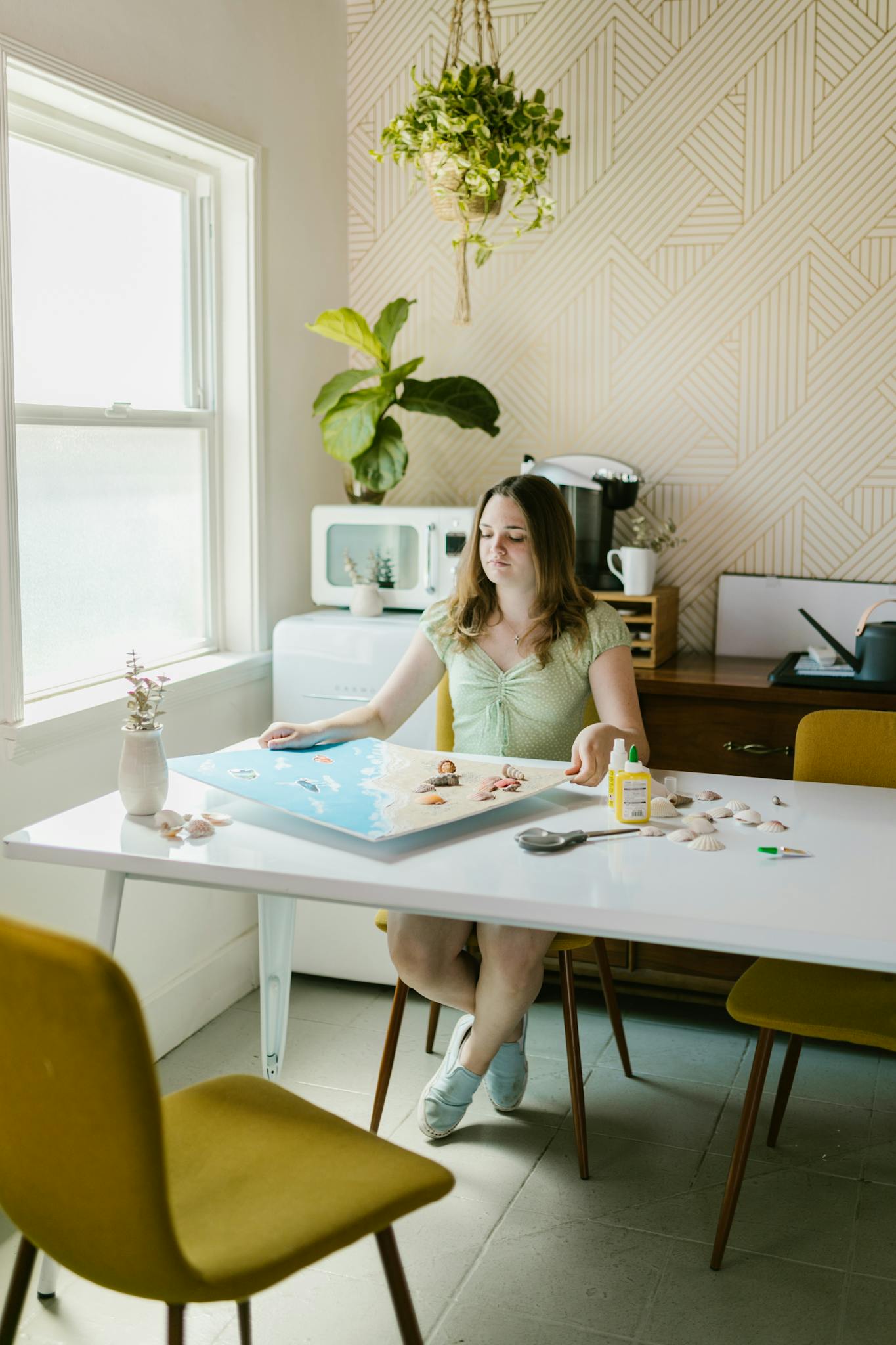A young woman enjoying a craft project at home in a bright, stylish kitchen setting.
